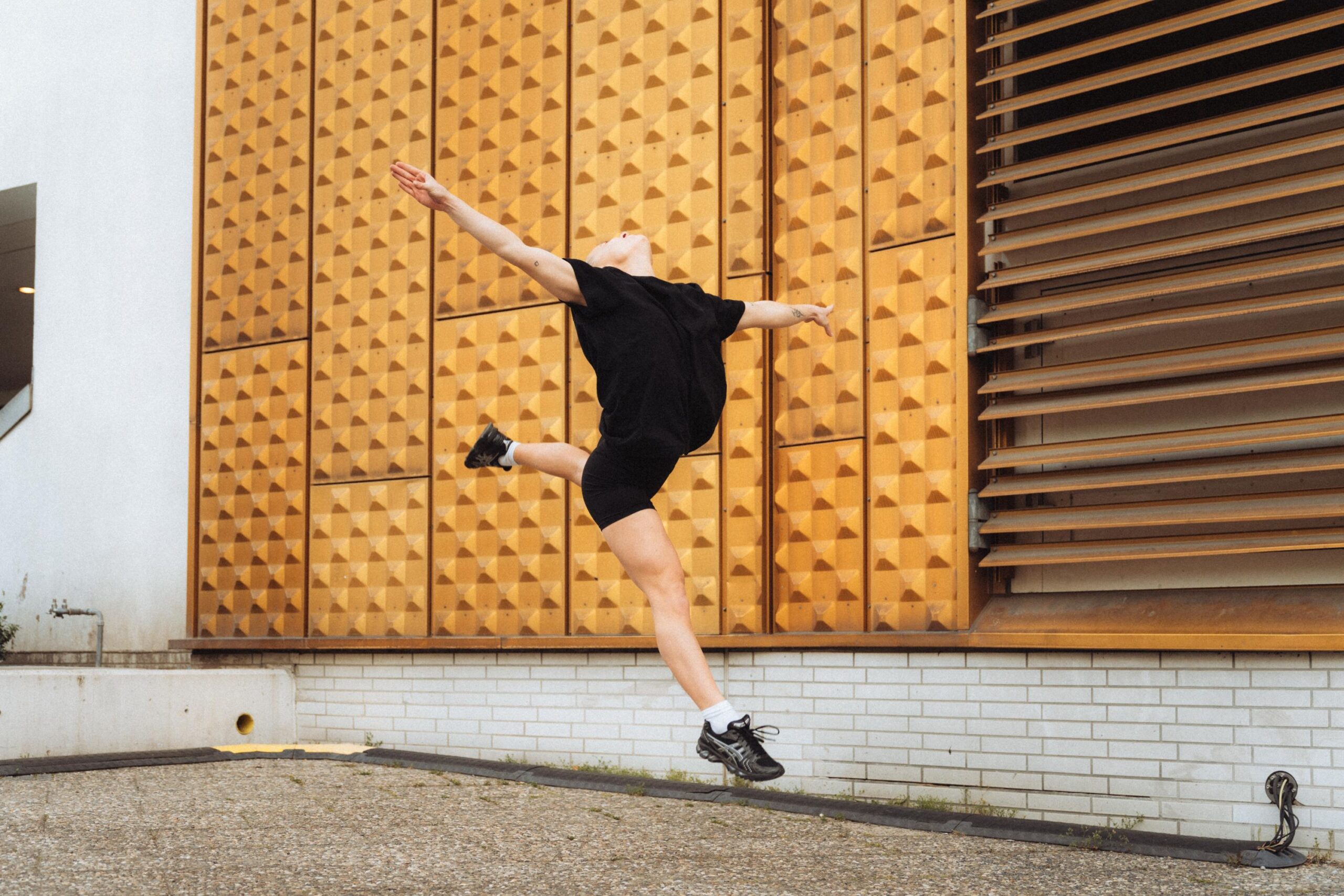 High-energy dance leap against modern architectural background.